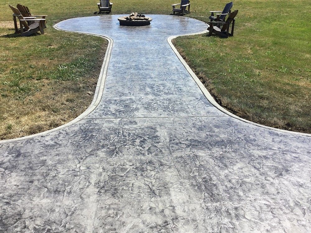 A concrete walkway leading to a fire pit in the middle of a grassy field.