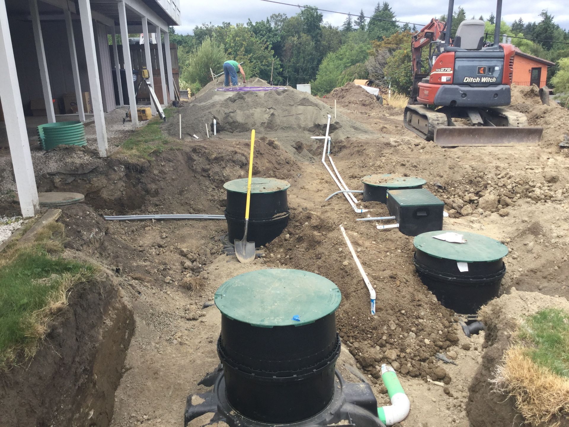 A large excavator is digging a hole in the dirt in front of a house.