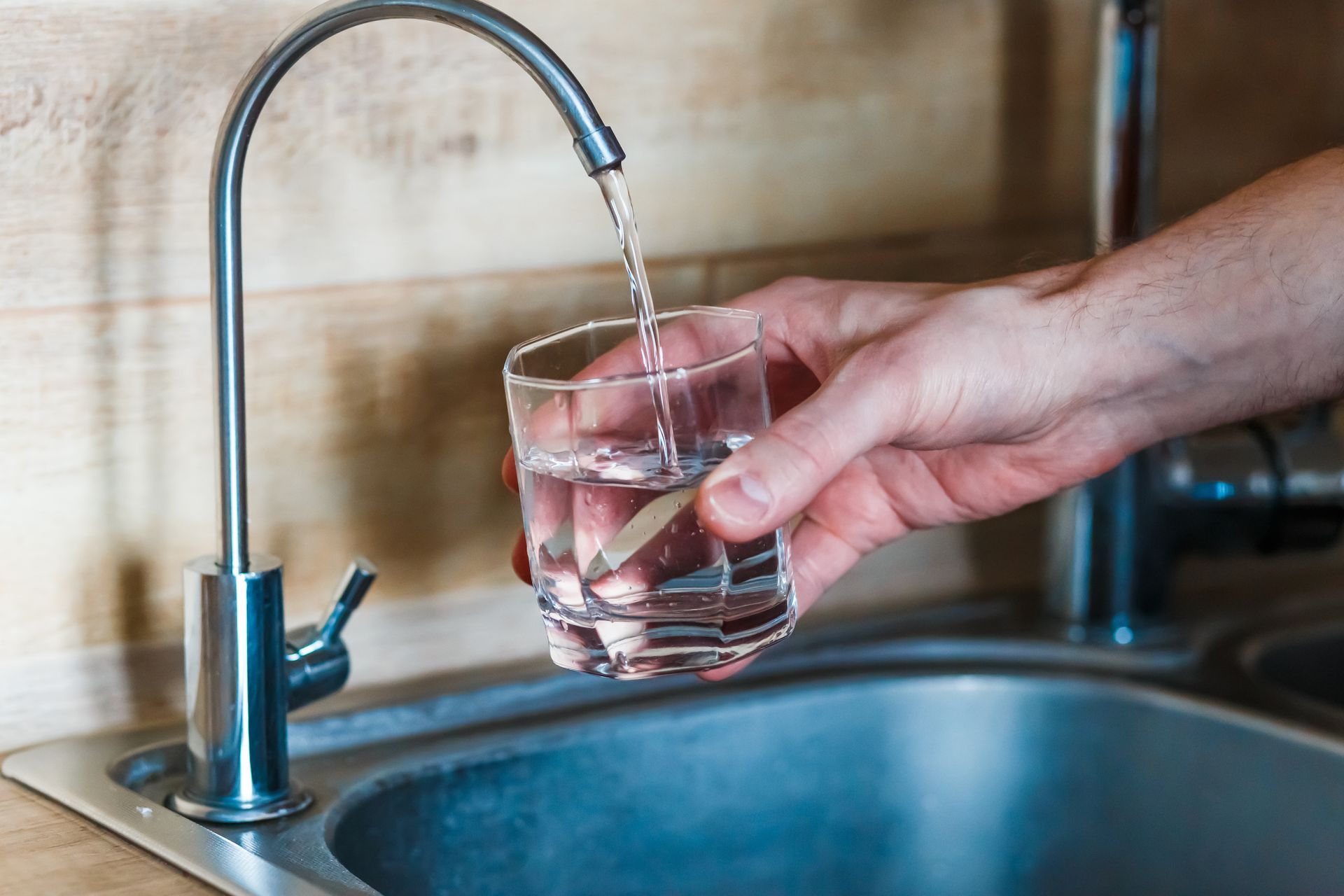 Hand filling a clear glass with water from a kitchen faucet.