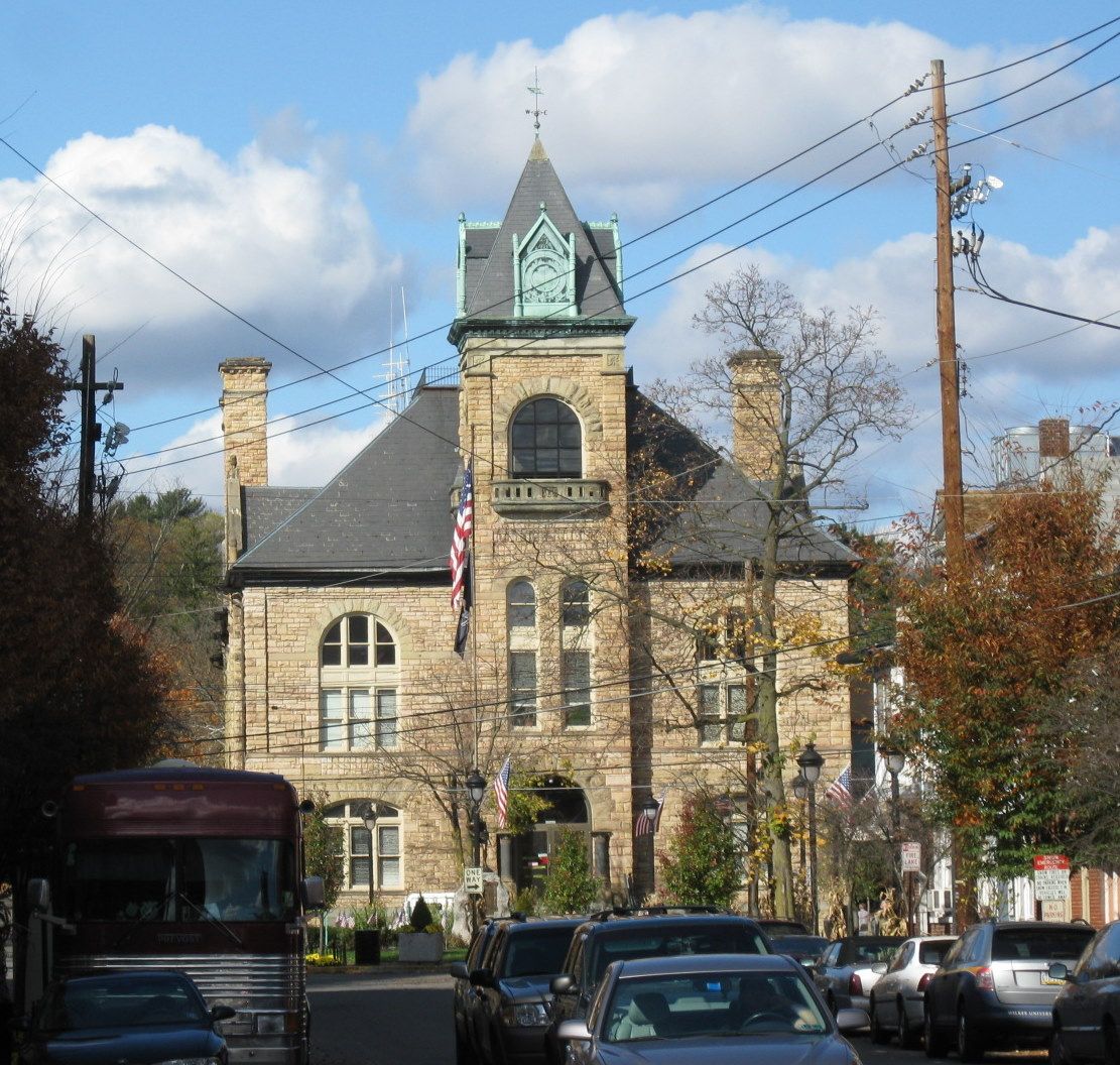 Historic stone building with a tower and flag, street scene with cars.