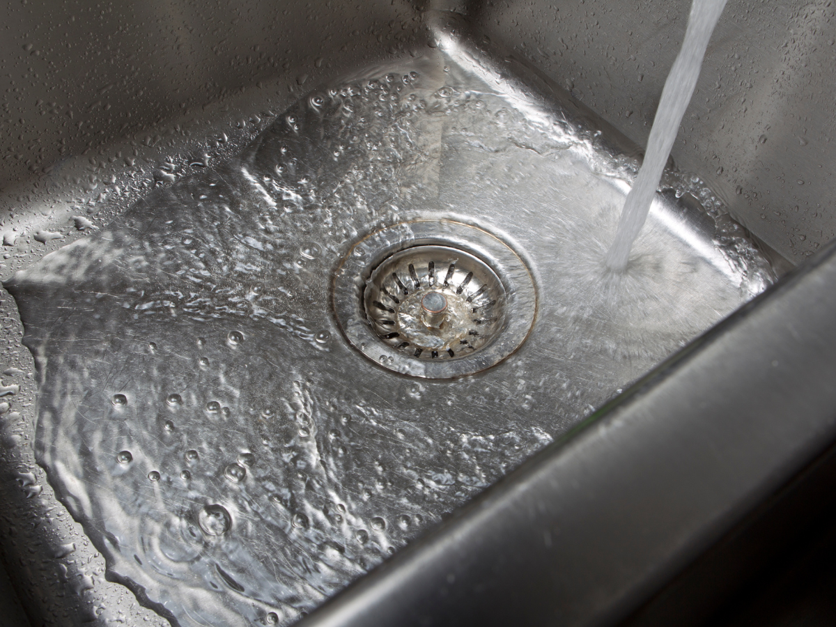 A stainless steel kitchen sink with water running down the drain.