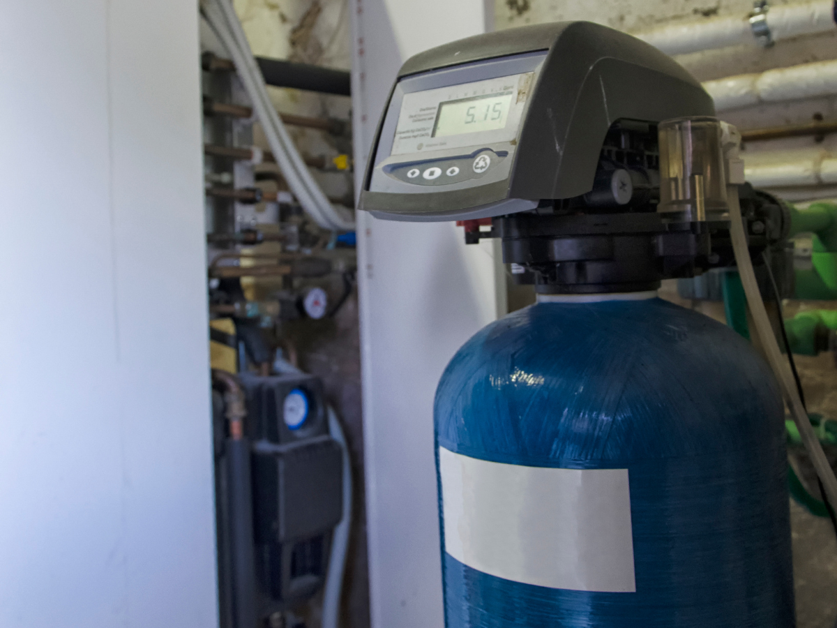 Blue water softener tank with digital display, installed in a utility room. Blue water softener tank with digital display, installed in a utility room.