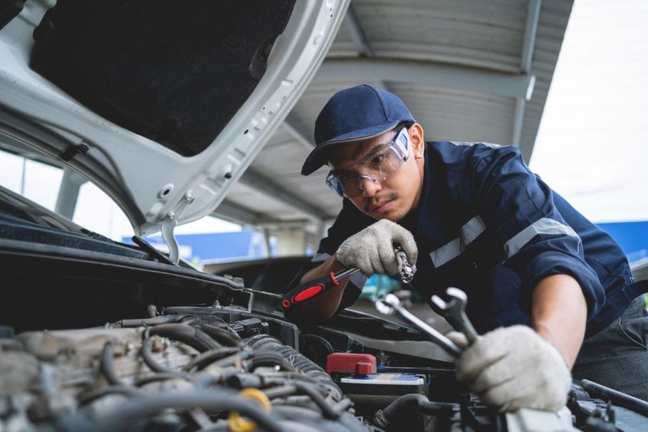 Mechanic using a wrench to repair a car engine under an open hood in a garage