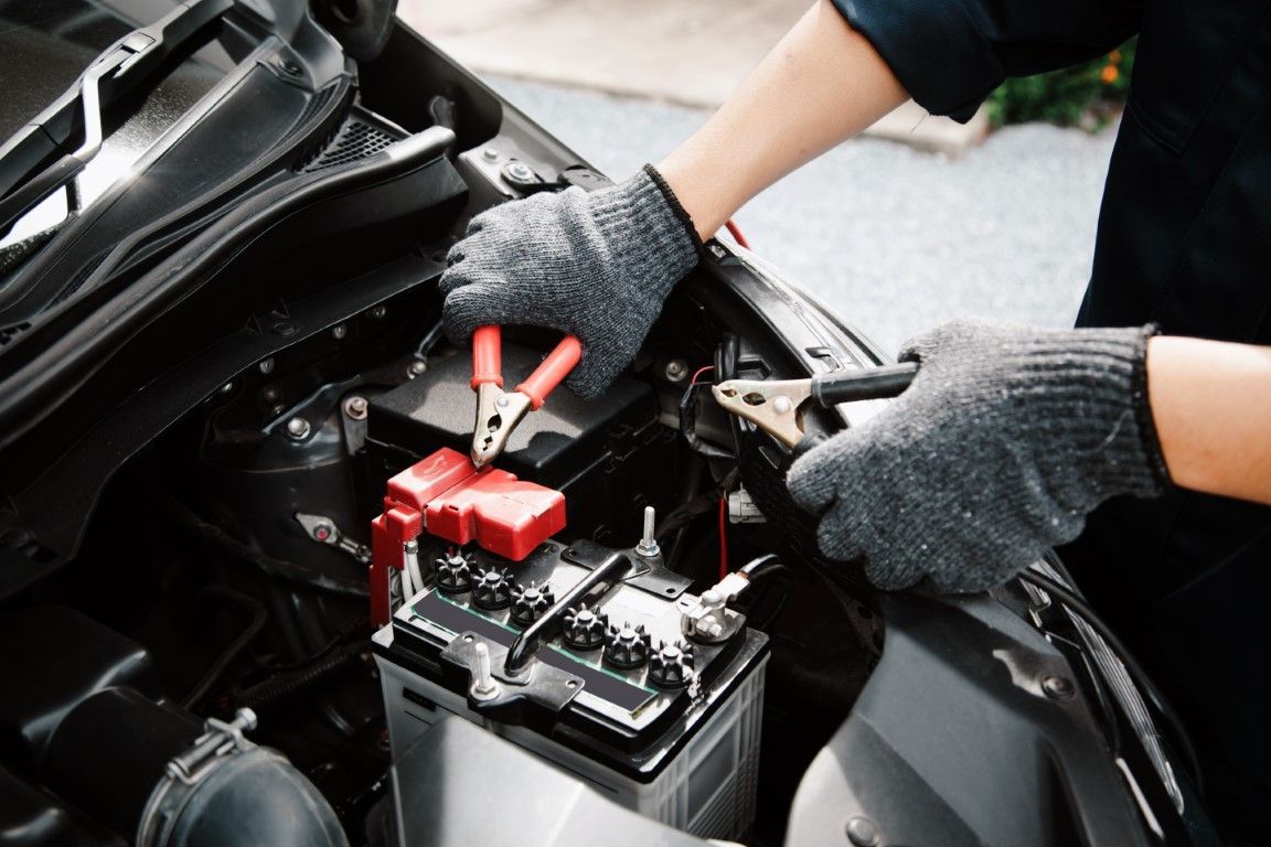 Mechanic charging a car battery with red jumper cables under the hood
