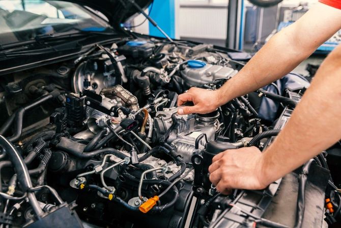 Mechanic working on a car engine in a repair shop, hands over exposed engine components.