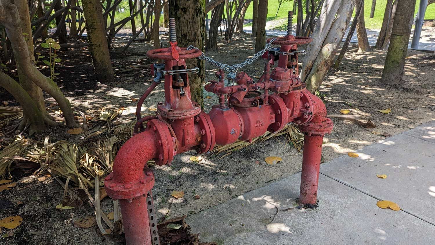 Red outdoor fire protection valves and pipes installed near trees beside a sidewalk path. Red outdoor fire protection valves and pipes installed near trees beside a sidewalk path.