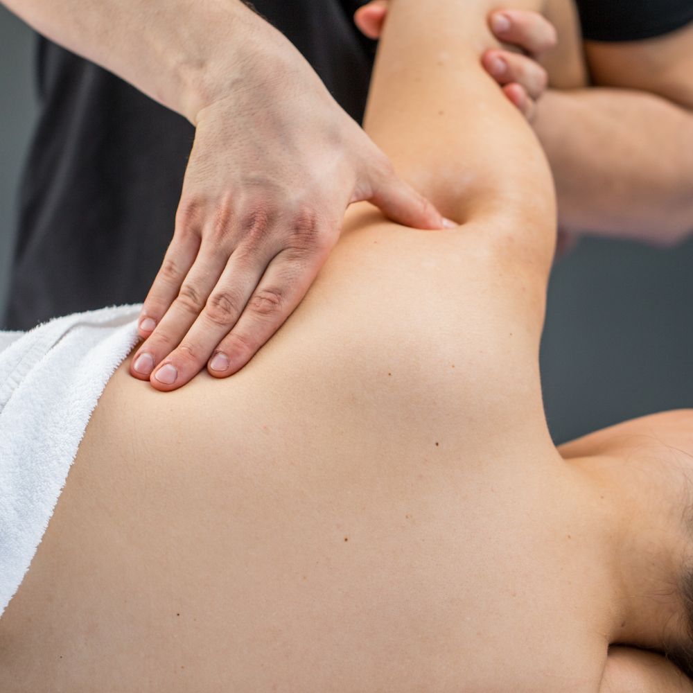 A therapist performs a shoulder massage on a person lying down.