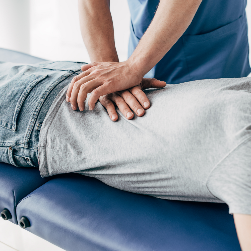 A physical therapist in blue scrubs performs a back adjustment on a person lying prone on a blue massage table.