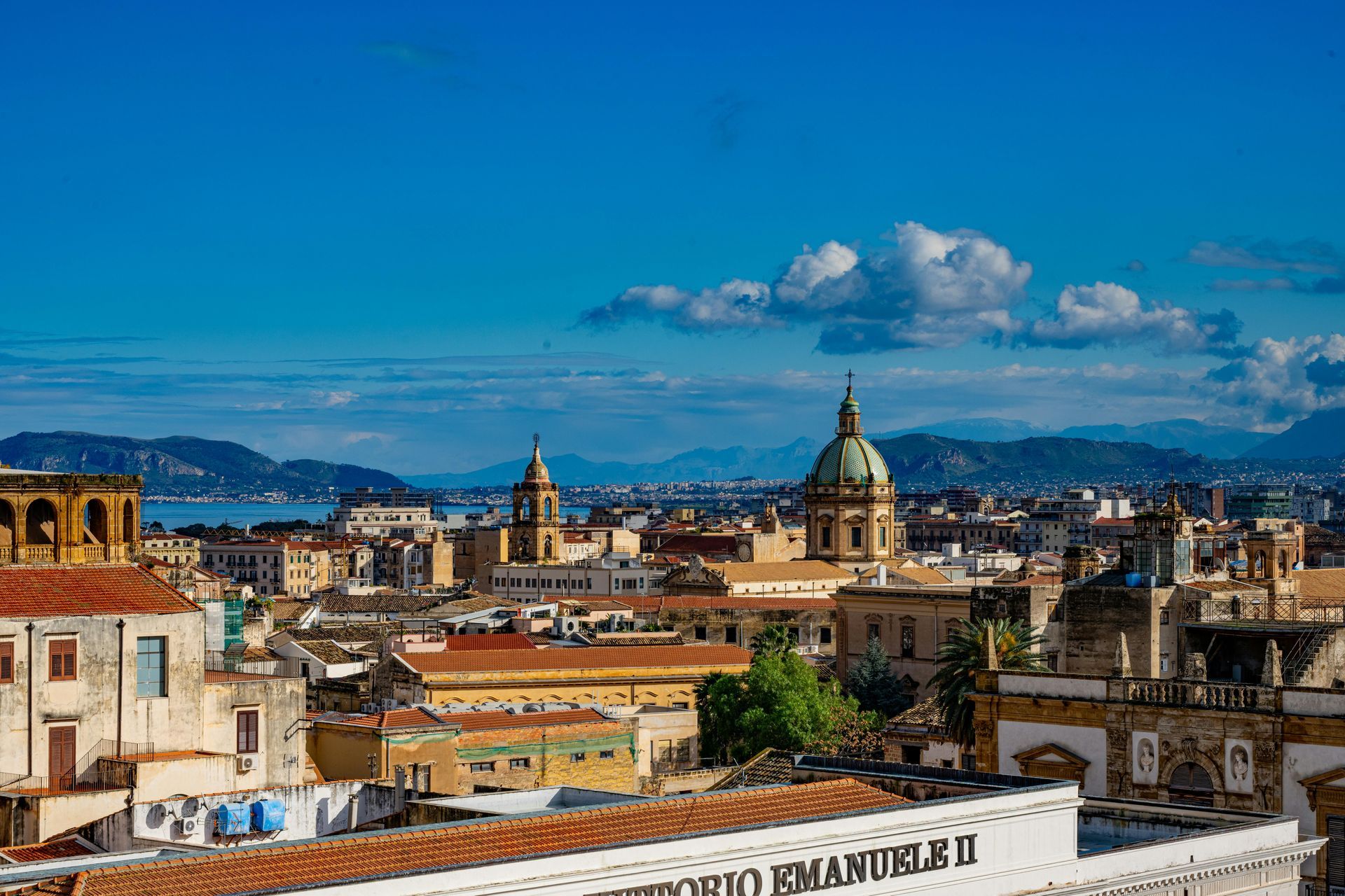 Panoramic cityscape with domed cathedral, historic buildings, and blue sky over distant hills