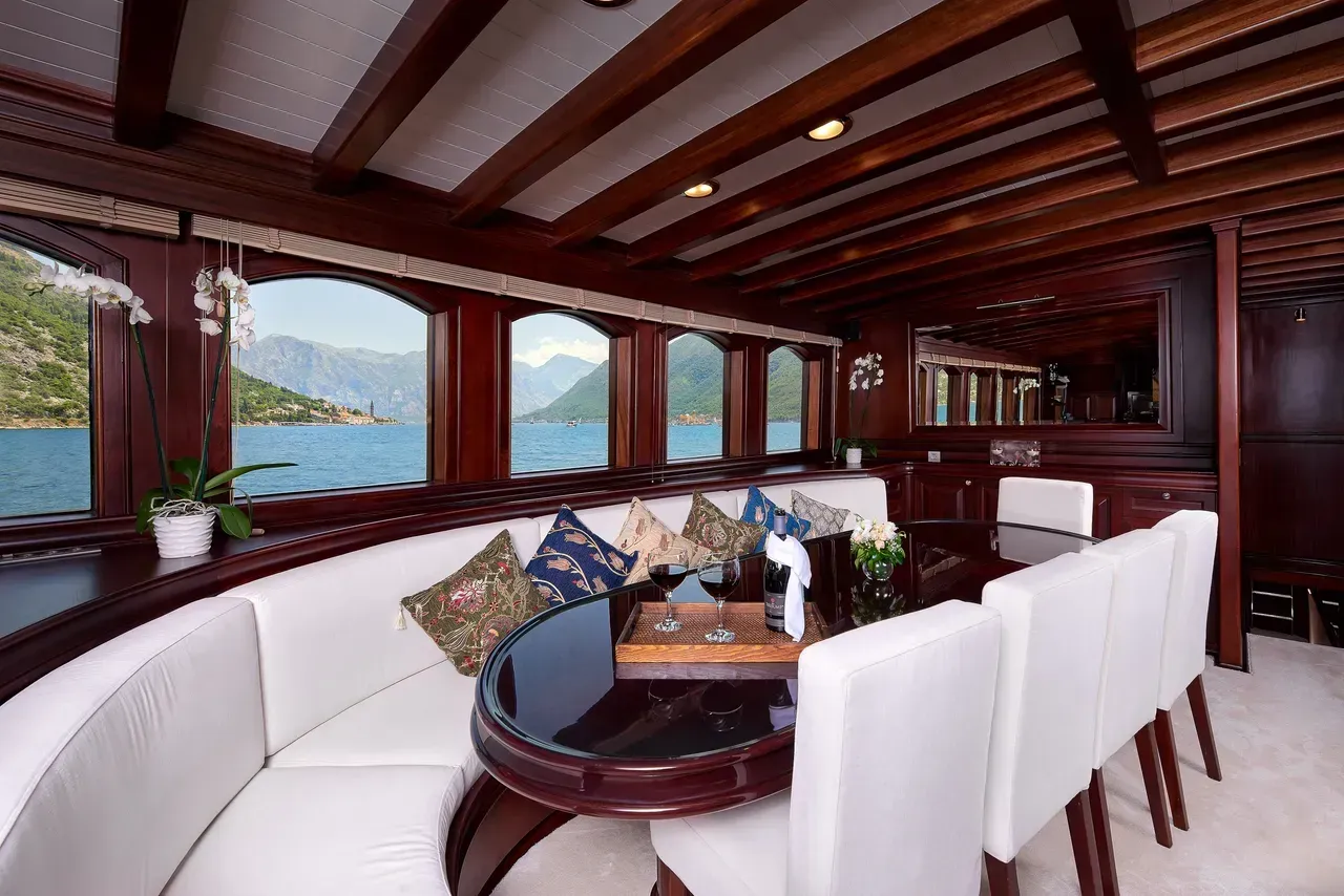 Elegant boat lounge with white curved seating, wooden beams, and ocean views through large windows