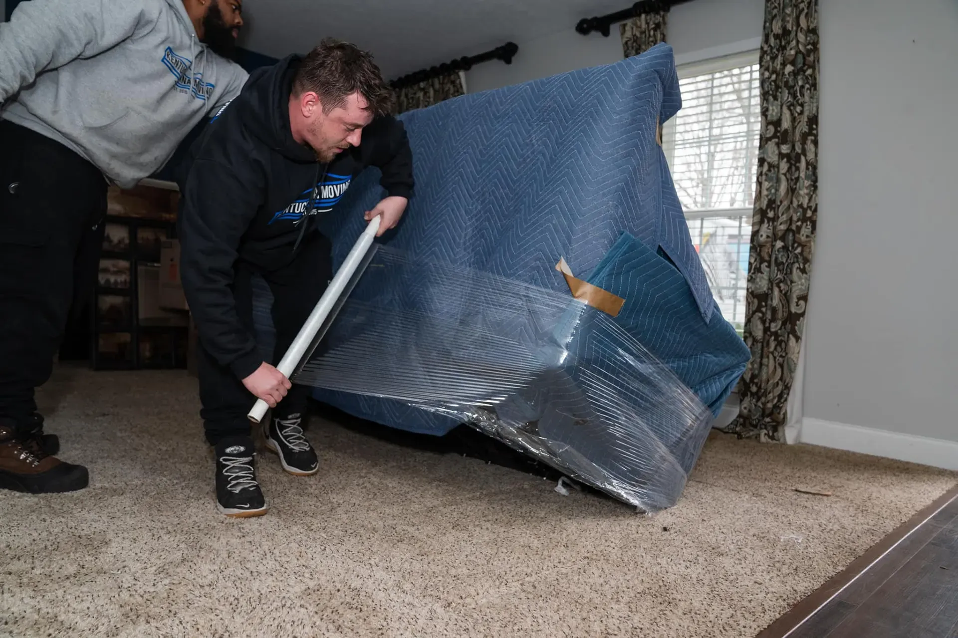 Two men are moving a piano in a living room.