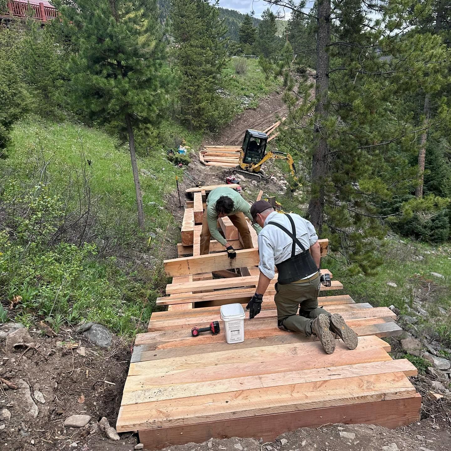 Workers building a wooden staircase trail on a steep forest hillside
