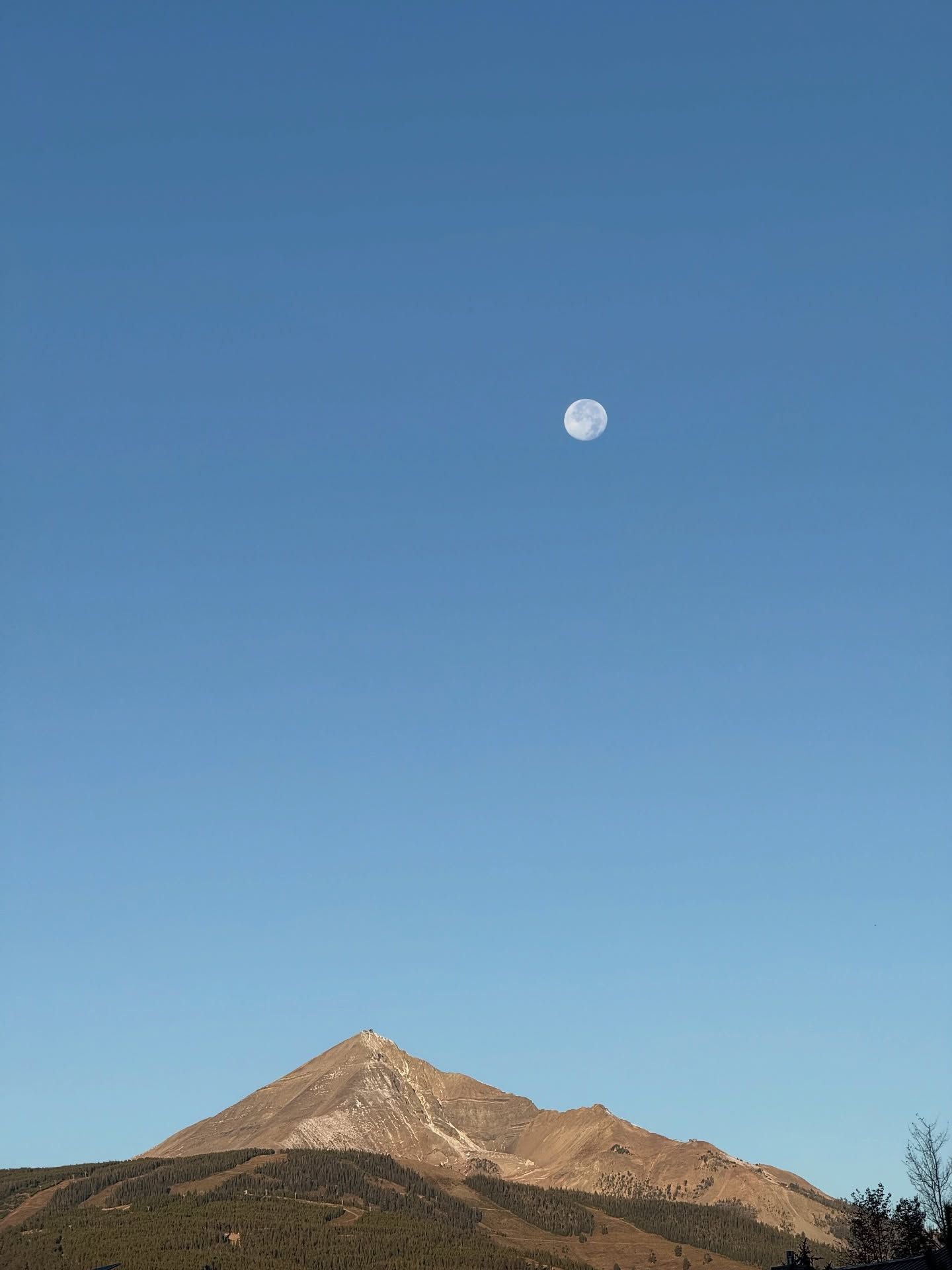 Moon above a rugged mountain ridge under a clear blue sky