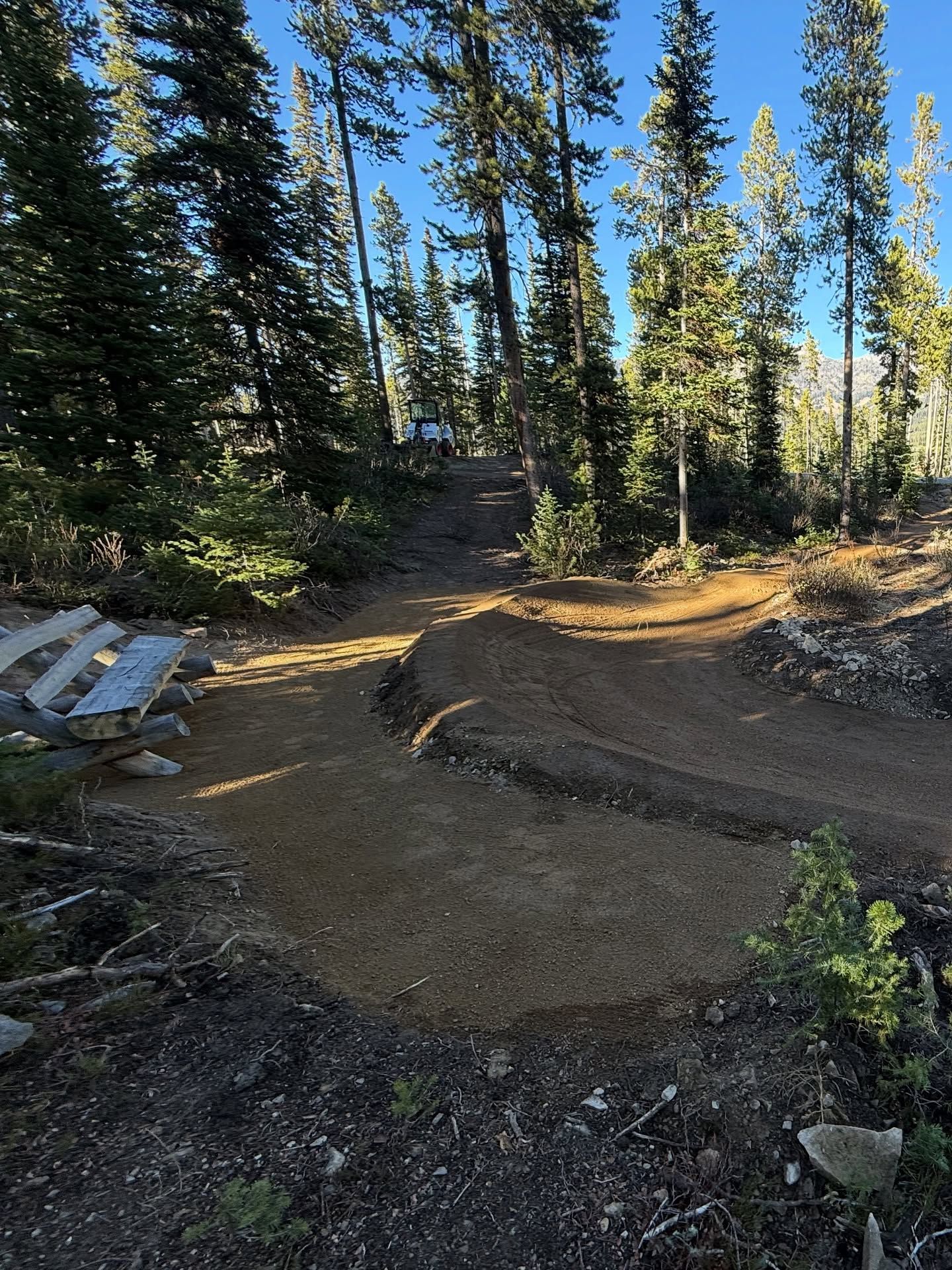 Dirt trail bike jump in a forest clearing with tall pine trees and scattered construction materials