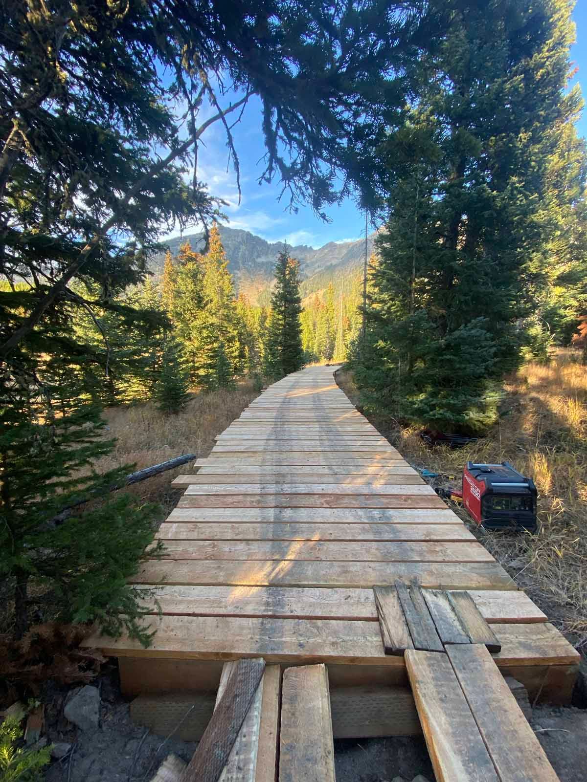 Wooden bridge trail through forest toward sunlit mountains, with a red box on the right.
