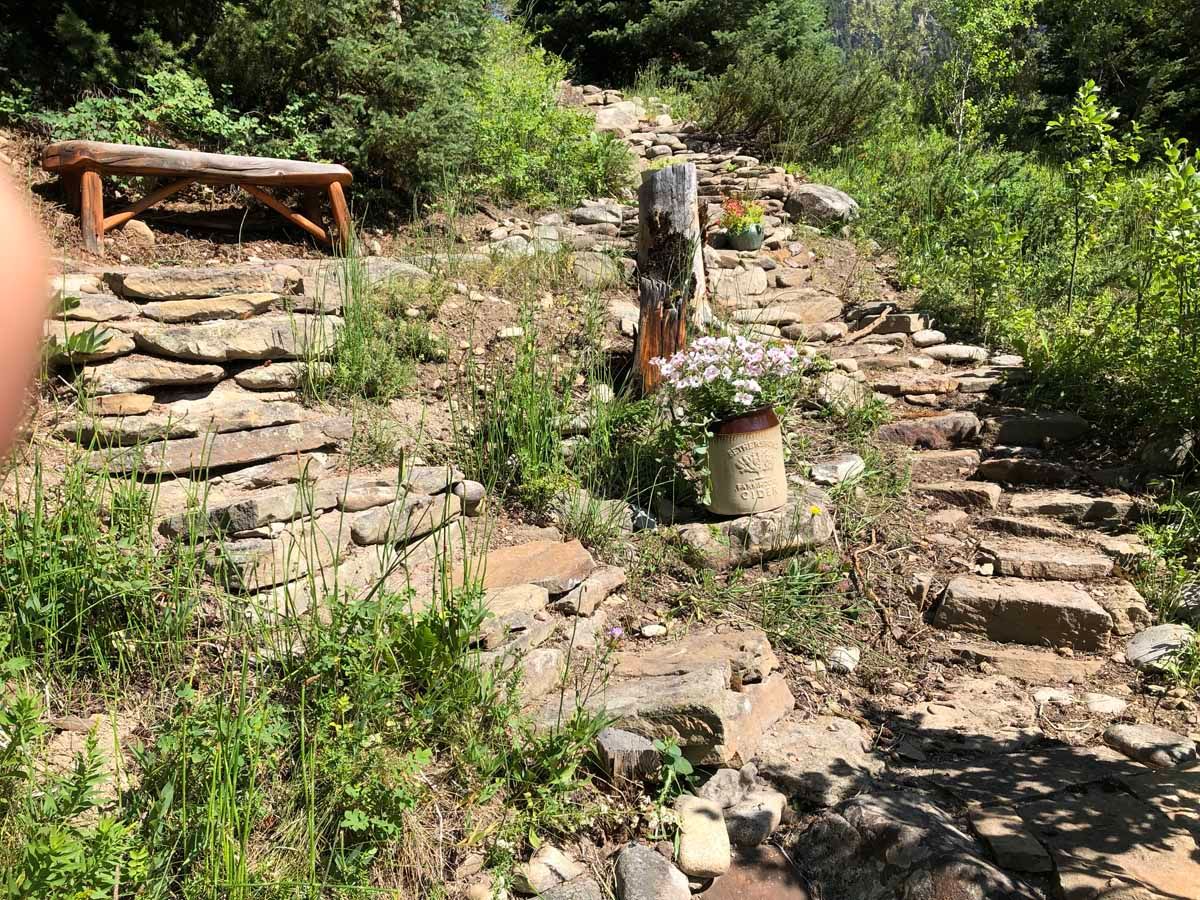 Stone steps and a retaining wall on a rocky hillside with green vegetation and a wooden bench.