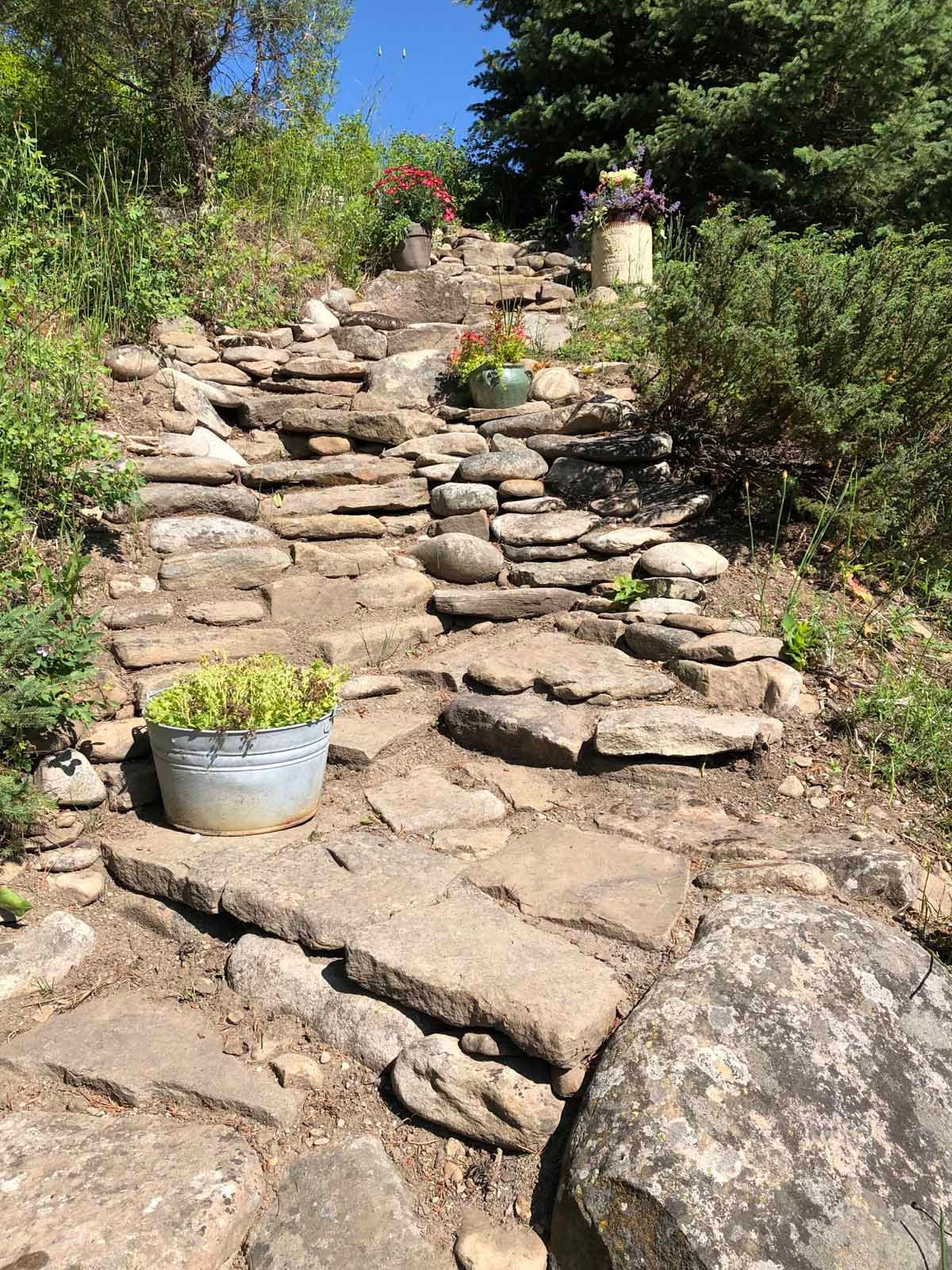 Stone garden steps with potted plants and greenery on a sunny hillside