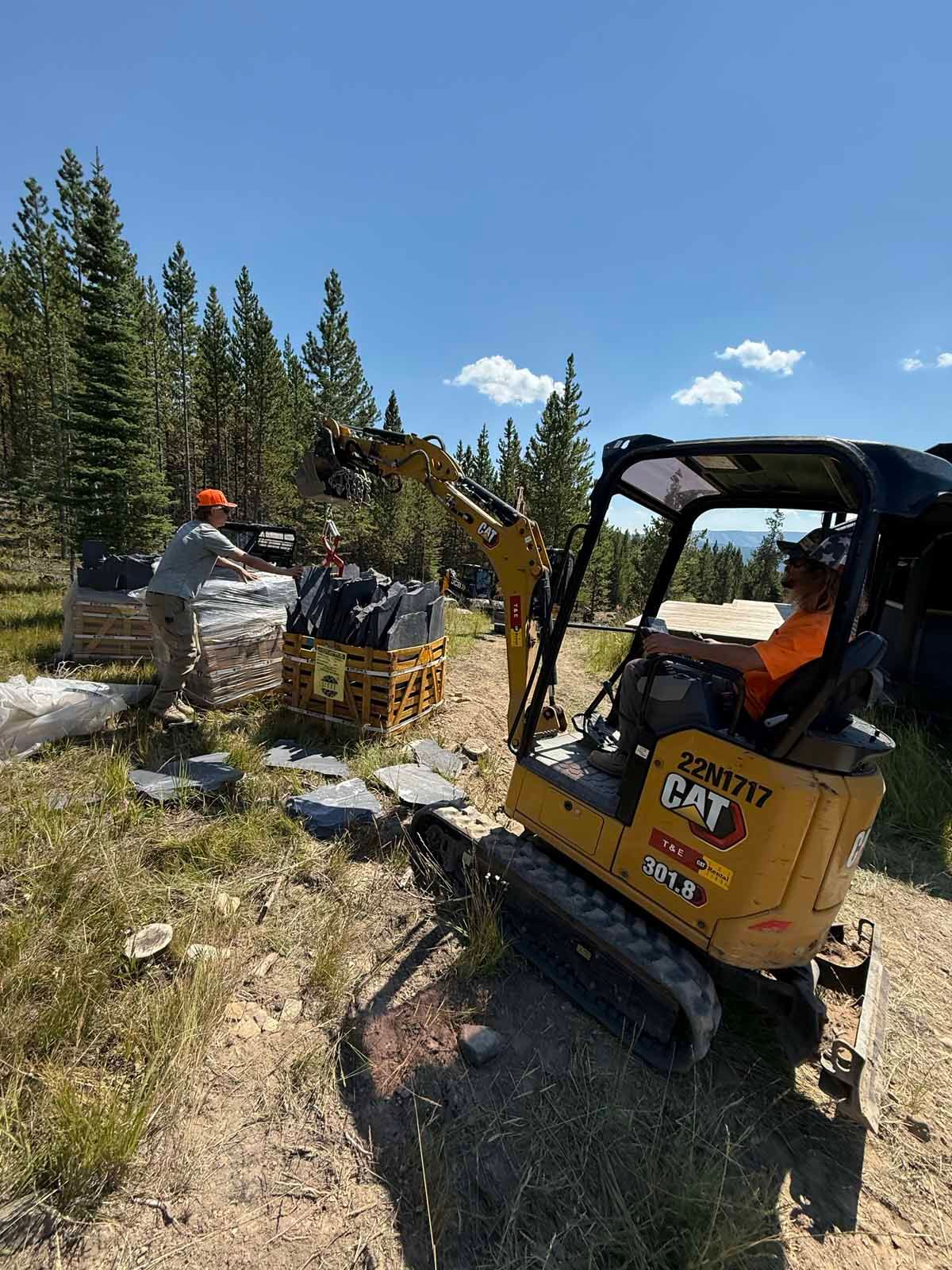 Yellow CAT skid steer on a rocky forest worksite under a blue sky