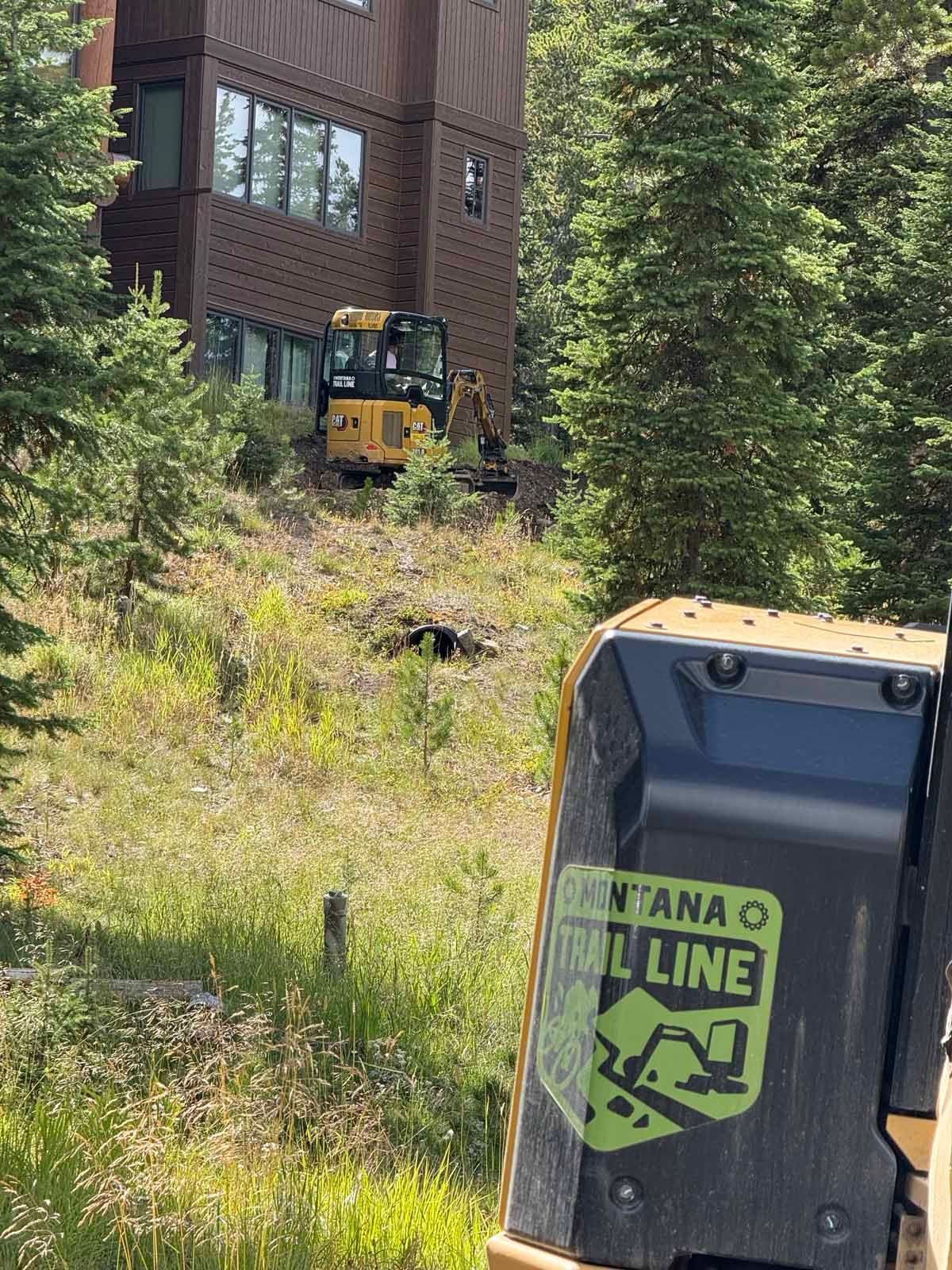 Yellow maintenance vehicle near a brick ski-lift building in a wooded mountain slope