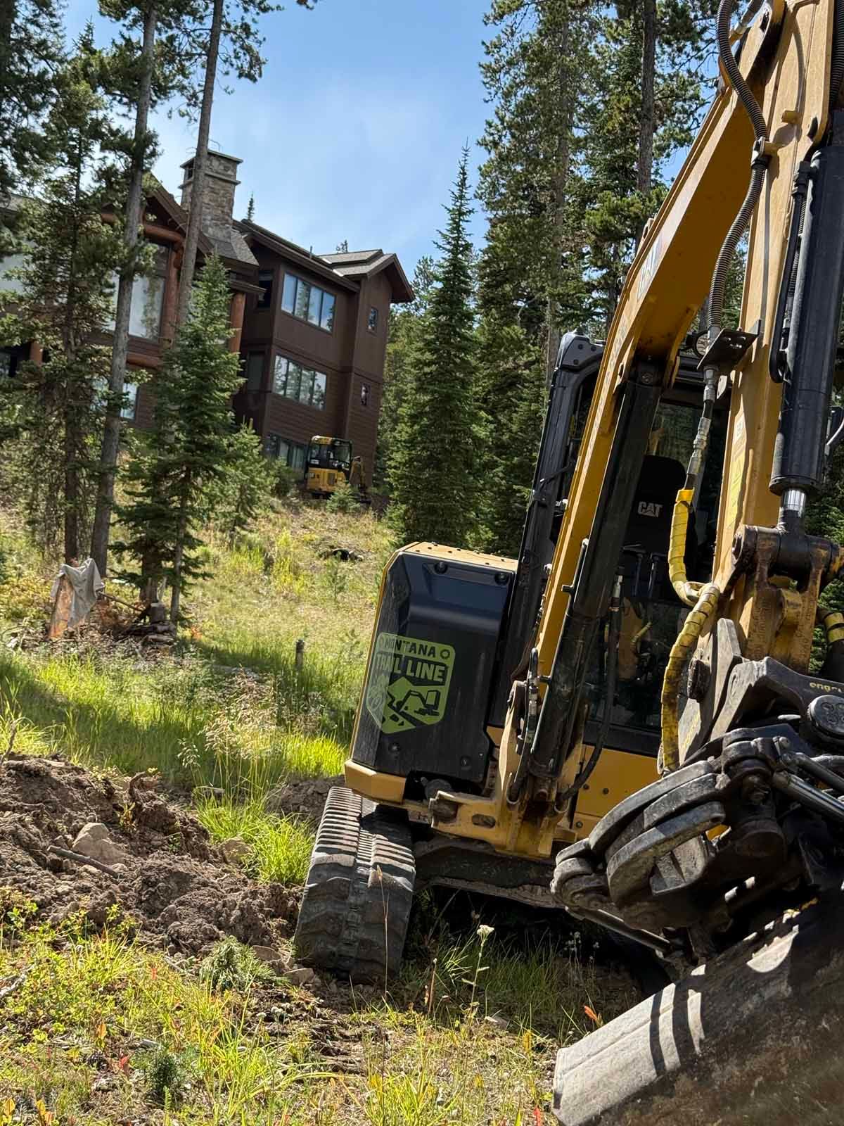 Excavator working beside a forest lodge in a wooded mountain area