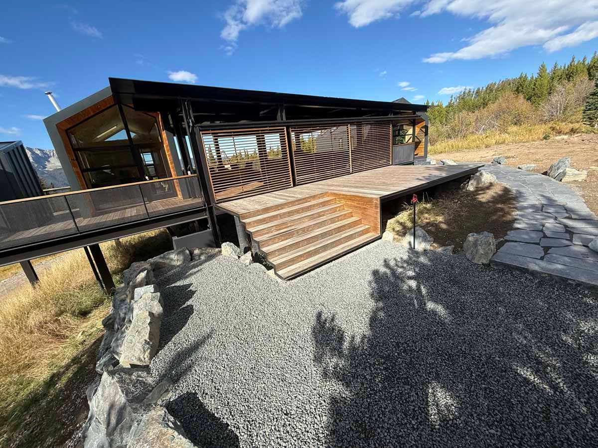 Modern house with a wooden deck and gravel landscaping on a sunny hillside