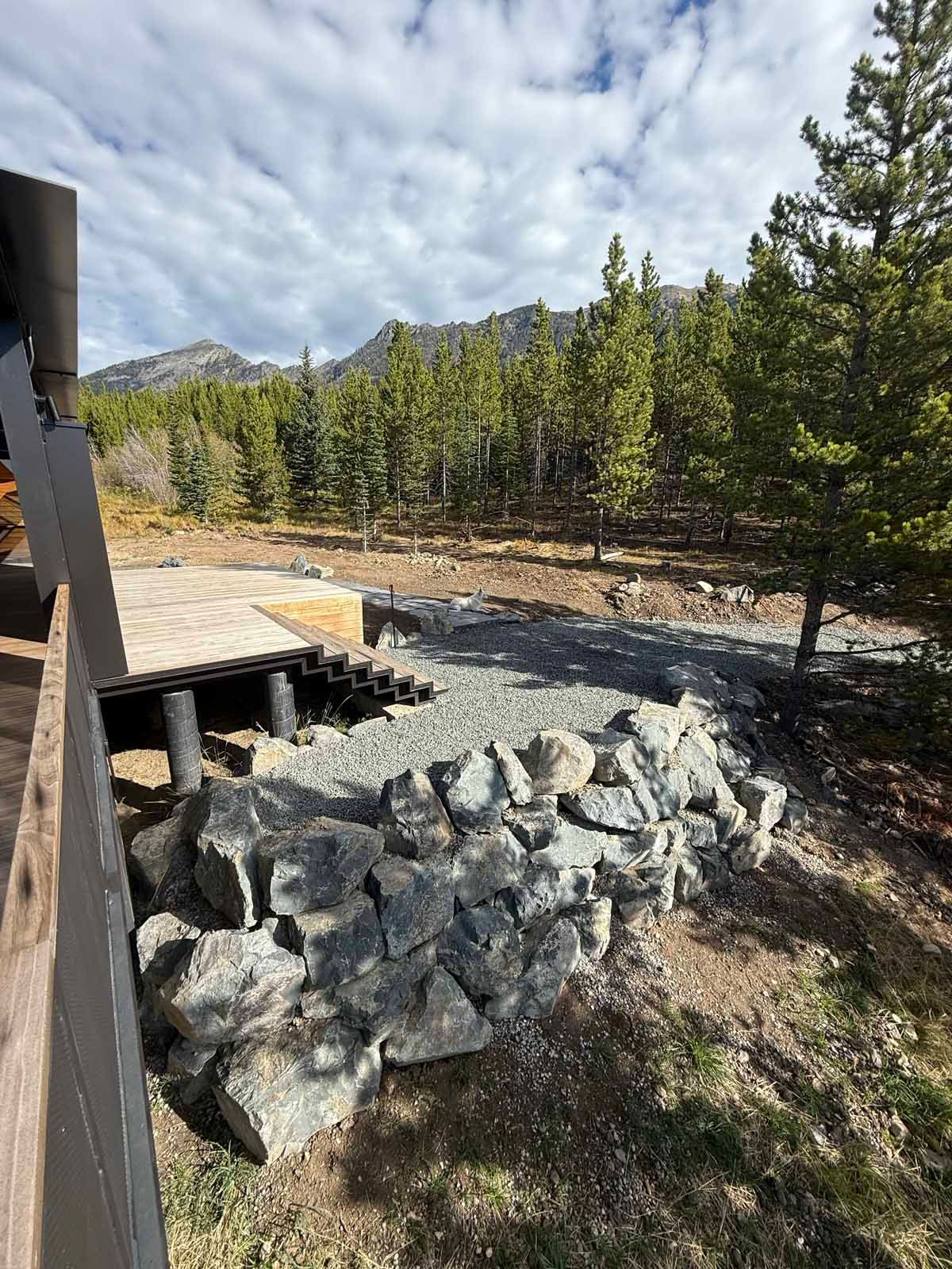 Rock retaining wall beside a wooden deck in a pine forest under a cloudy sky