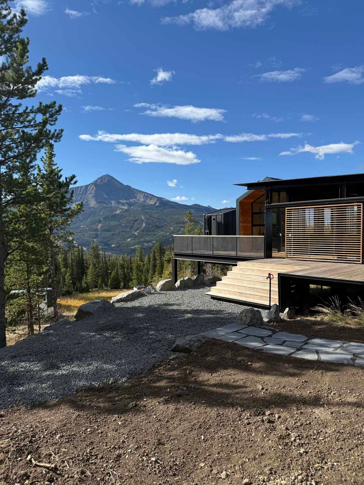 Cabin deck with stone path and pine trees overlooking a mountain under a blue sky