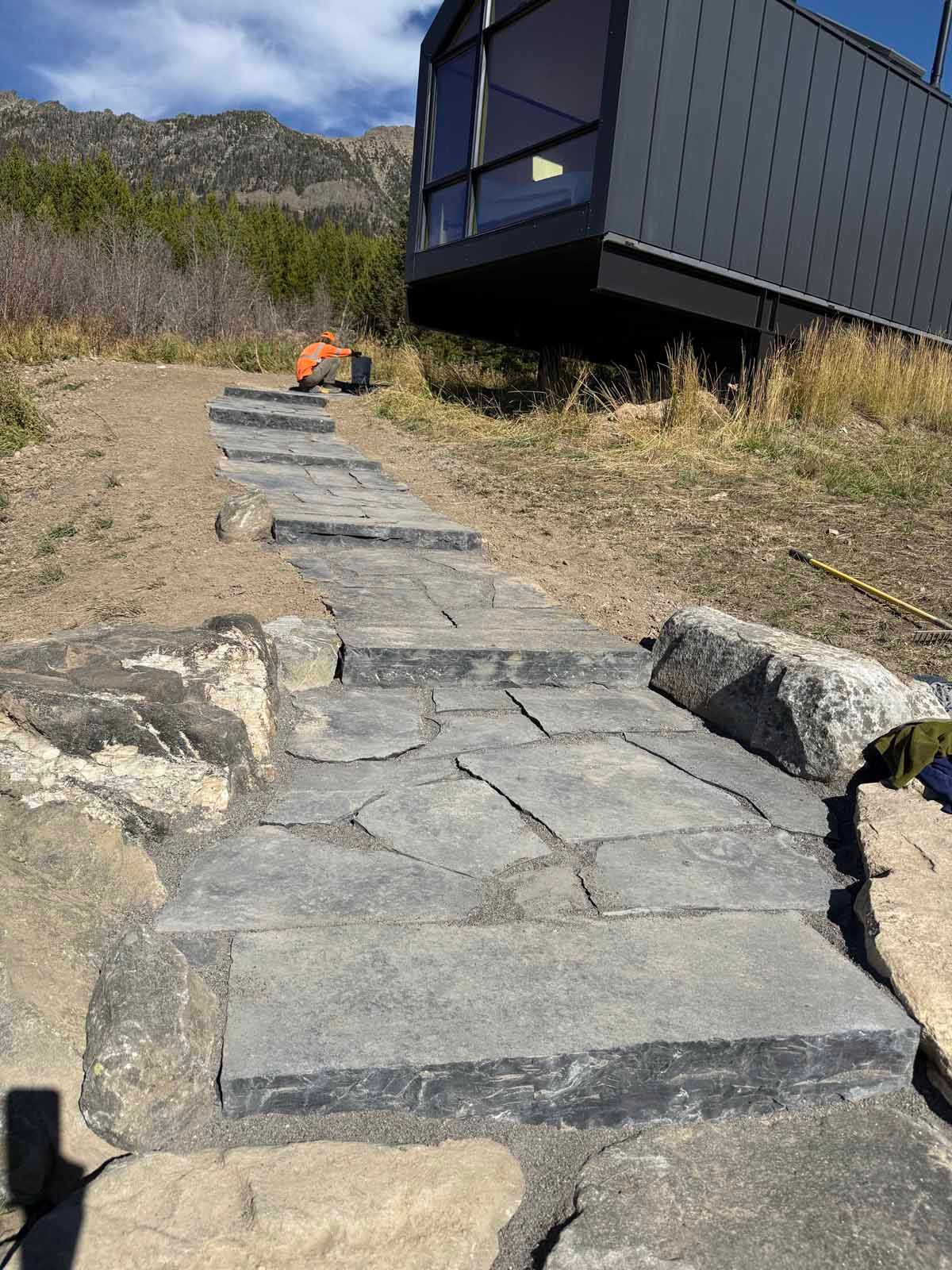Stone steps on a hillside leading to a modern cabin, with a small orange object near the top.