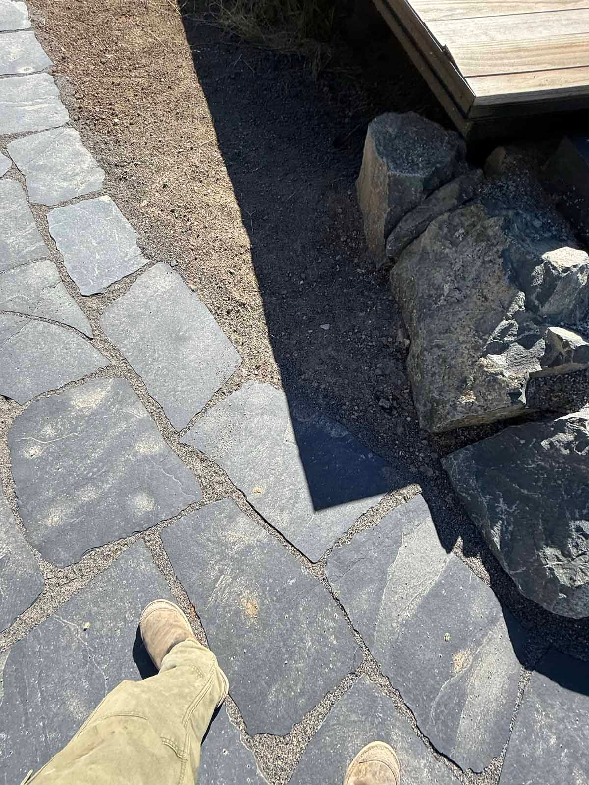 Stone pathway beside a dark water feature, with a pointing hand indicating the edge.