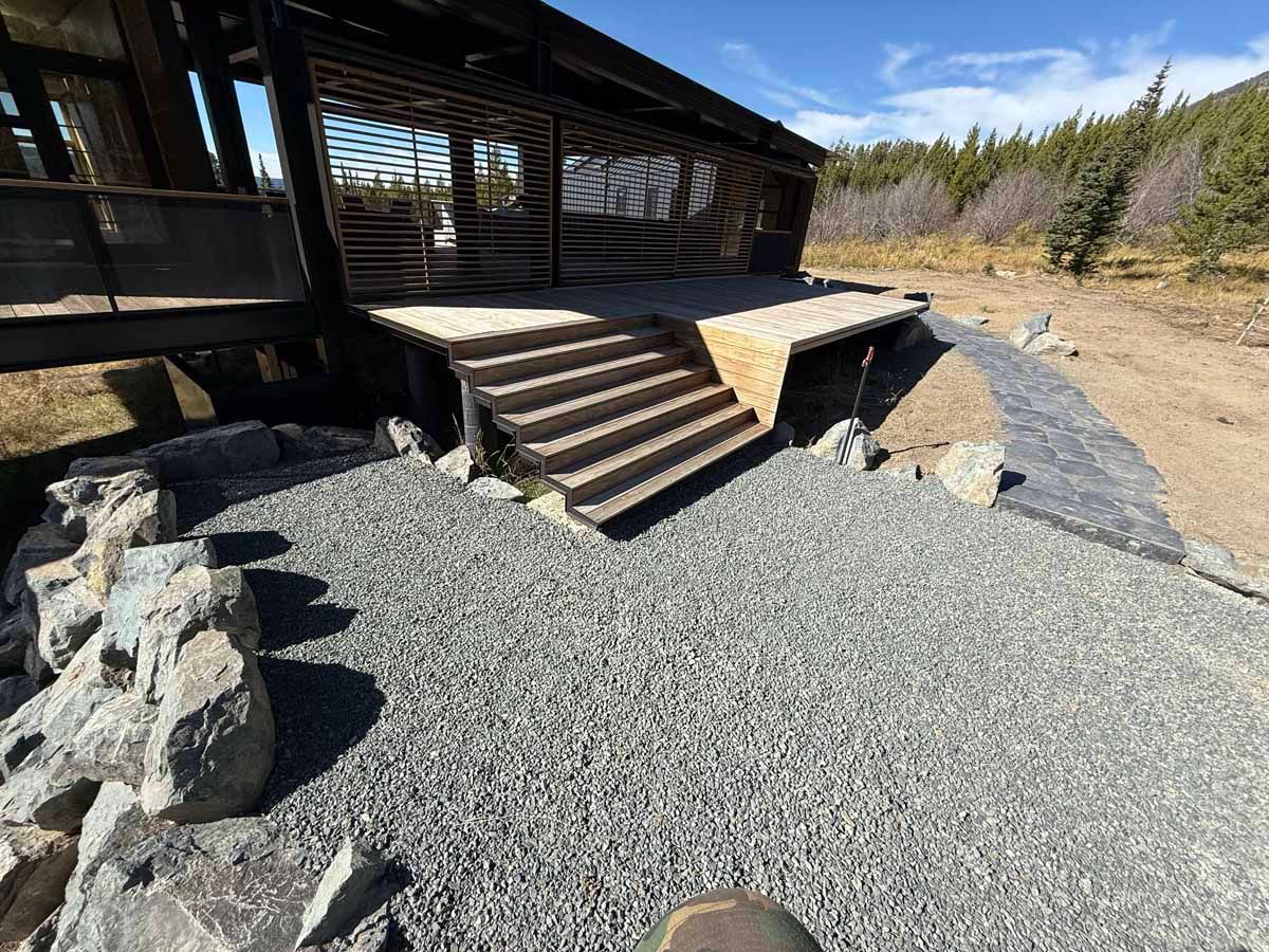 Rustic cabin porch with wooden steps beside a gravel landscape and rocky landscaping