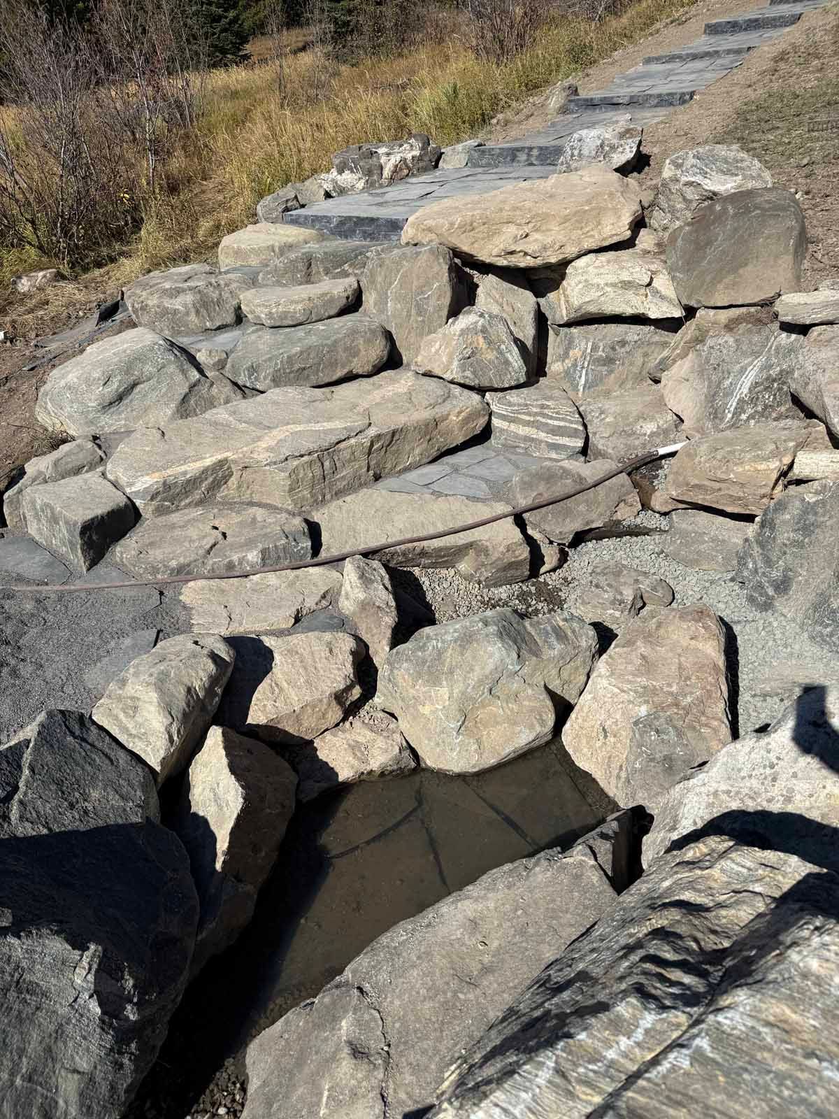 Stacked gray rocks forming a rough stone wall beside a path in dry grassland.