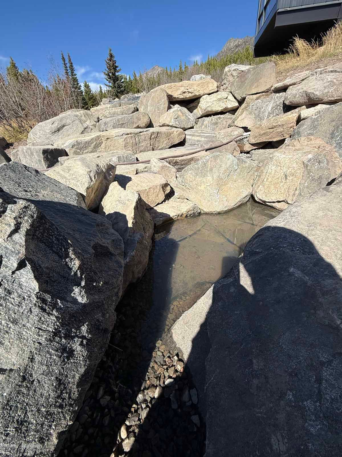 Stone retaining wall with a small rocky water feature and sunlight shadows outdoors