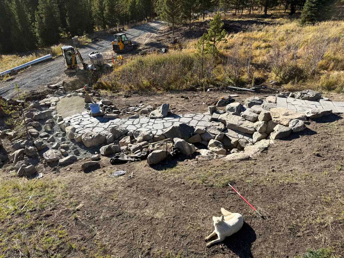 Stone fire pit ruins in a dry field with scattered rocks and a forested hillside beyond.