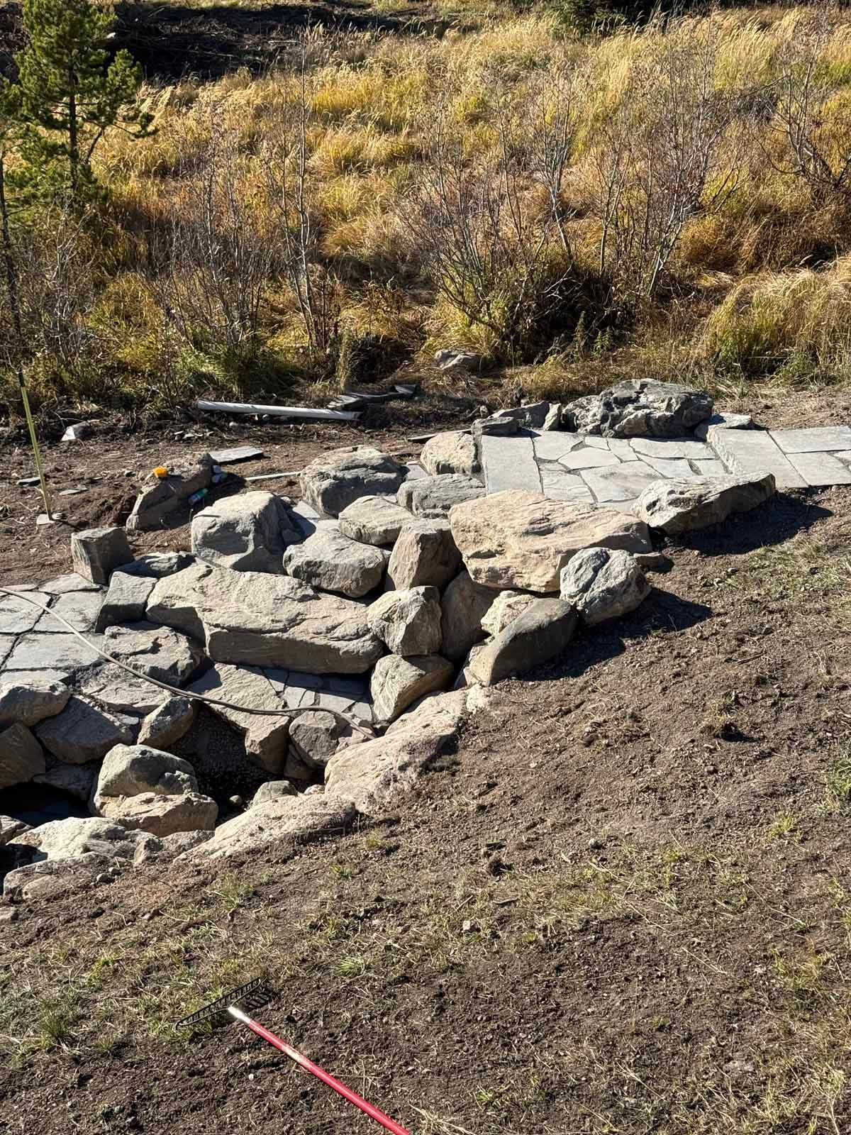 Rock retaining wall in a dry, grassy outdoor area with a red stake in the foreground.