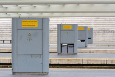 Gray electrical cabinets with yellow warning signs on a station platform