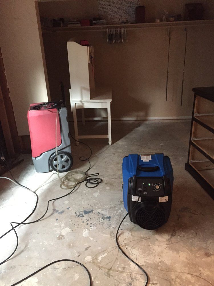 Two dehumidifiers in a room with a concrete floor, likely drying the space.