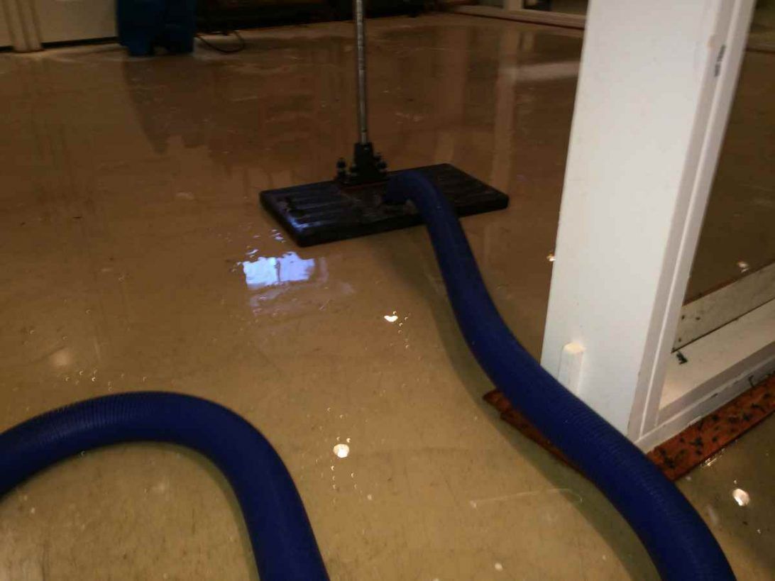 Blue hoses in muddy floodwater inside a room beside a wet mop and doorframe.