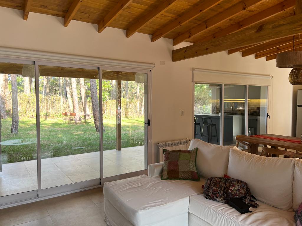 Sala de estar con puertas corredizas de vidrio que dan a un jardín con césped y árboles. 