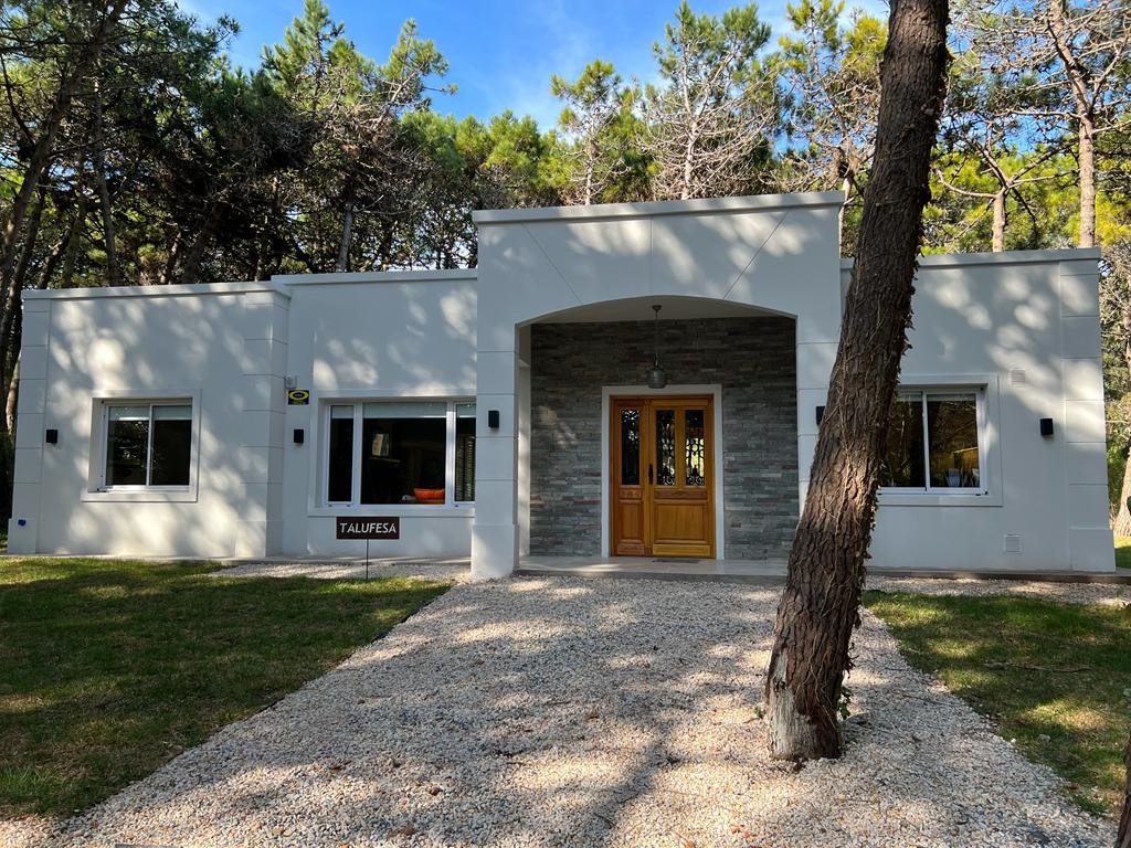 Casa blanca de una sola planta con entrada de piedra gris y sendero de grava. Un árbol se encuentra en primer plano.