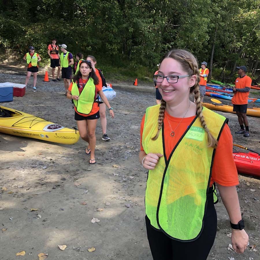 All Out Adventures volunteers in green vests help others with kayaks on a beach.