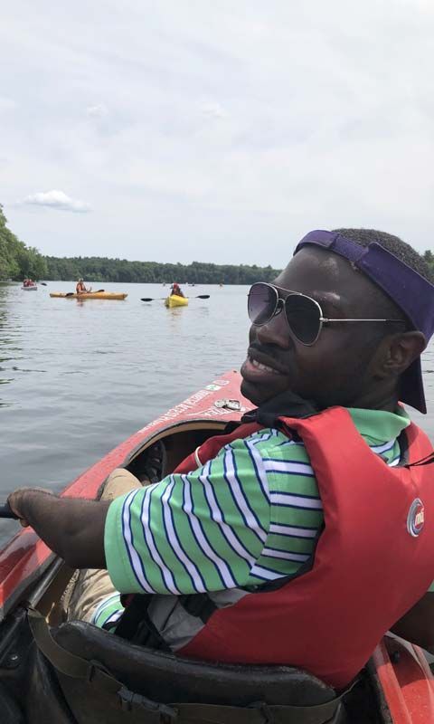 A kayak program participant in a lifejacket paddles his kayak and smiles at the camera.