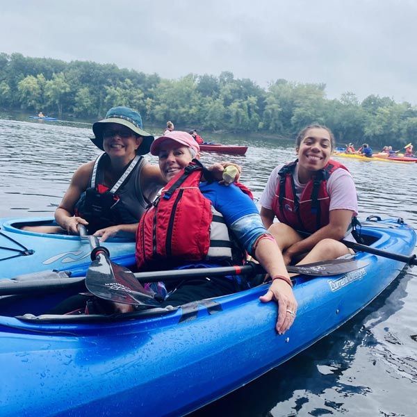 Three people are sitting and smiling in a pair of blue kayaks on the Connecticut River.