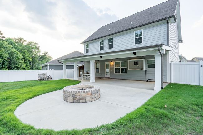 A backyard with a concrete patio, a stone fire pit, and a covered porch attached to the back of a two-story gray house.