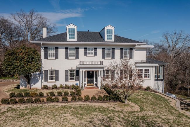 A white, two-story house with a black roof, symmetrical windows, and a small front porch under a clear blue sky.