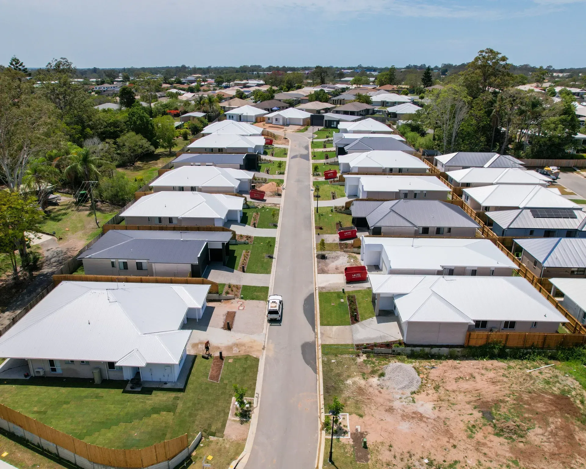 Aerial view of a new residential street lined with modern, light-roofed suburban houses under a clear blue sky.