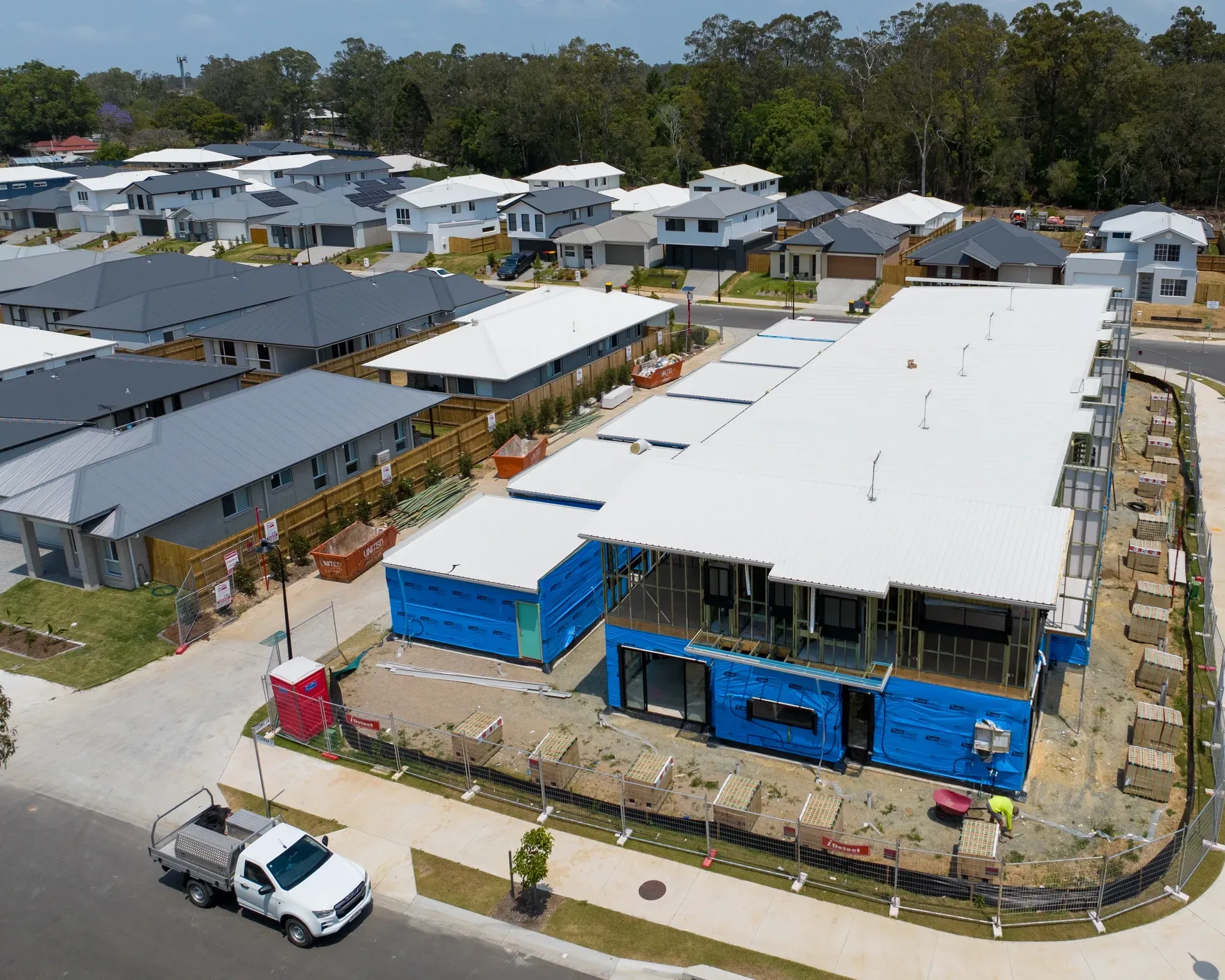 Aerial view of a construction site with several new houses in the background. A white work truck is parked in the street. — Smart Metal Roofing in Coomera, QLD