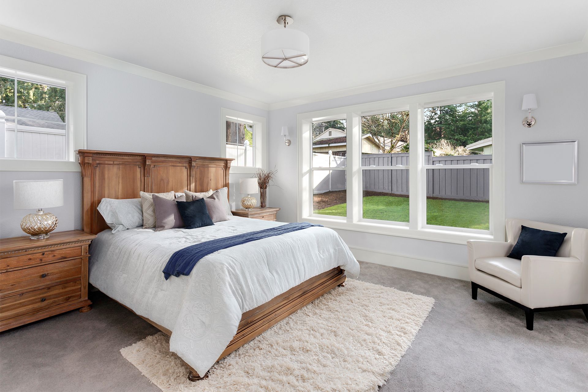 A bedroom with a bed , chair , nightstand and windows.