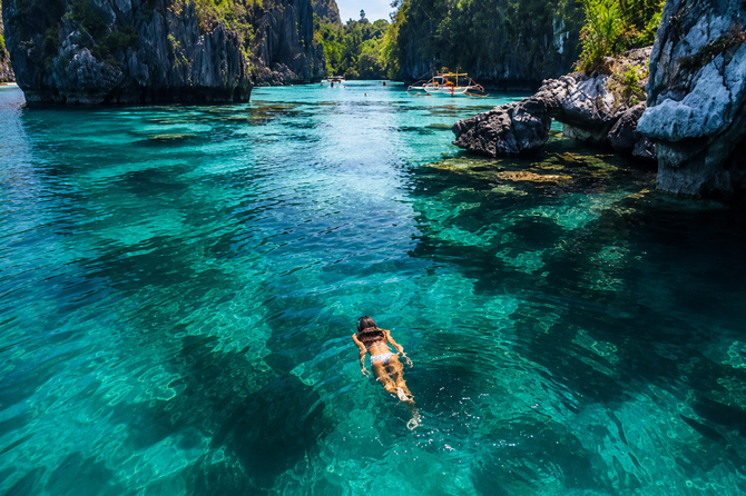 Swimmer floating in clear turquoise lagoon between rocky cliffs and lush green trees