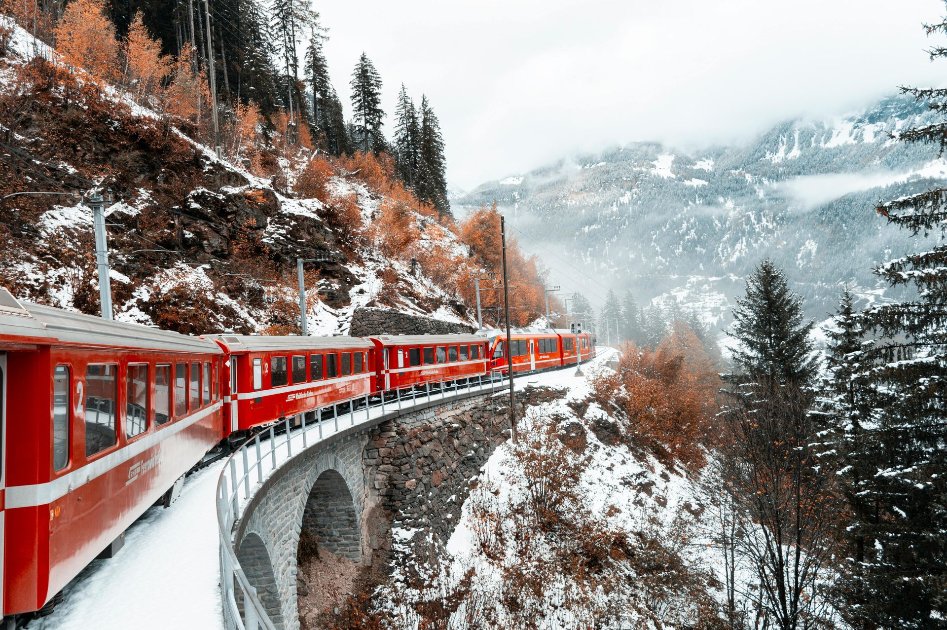 Red train crossing a snowy mountain viaduct through a winter forest