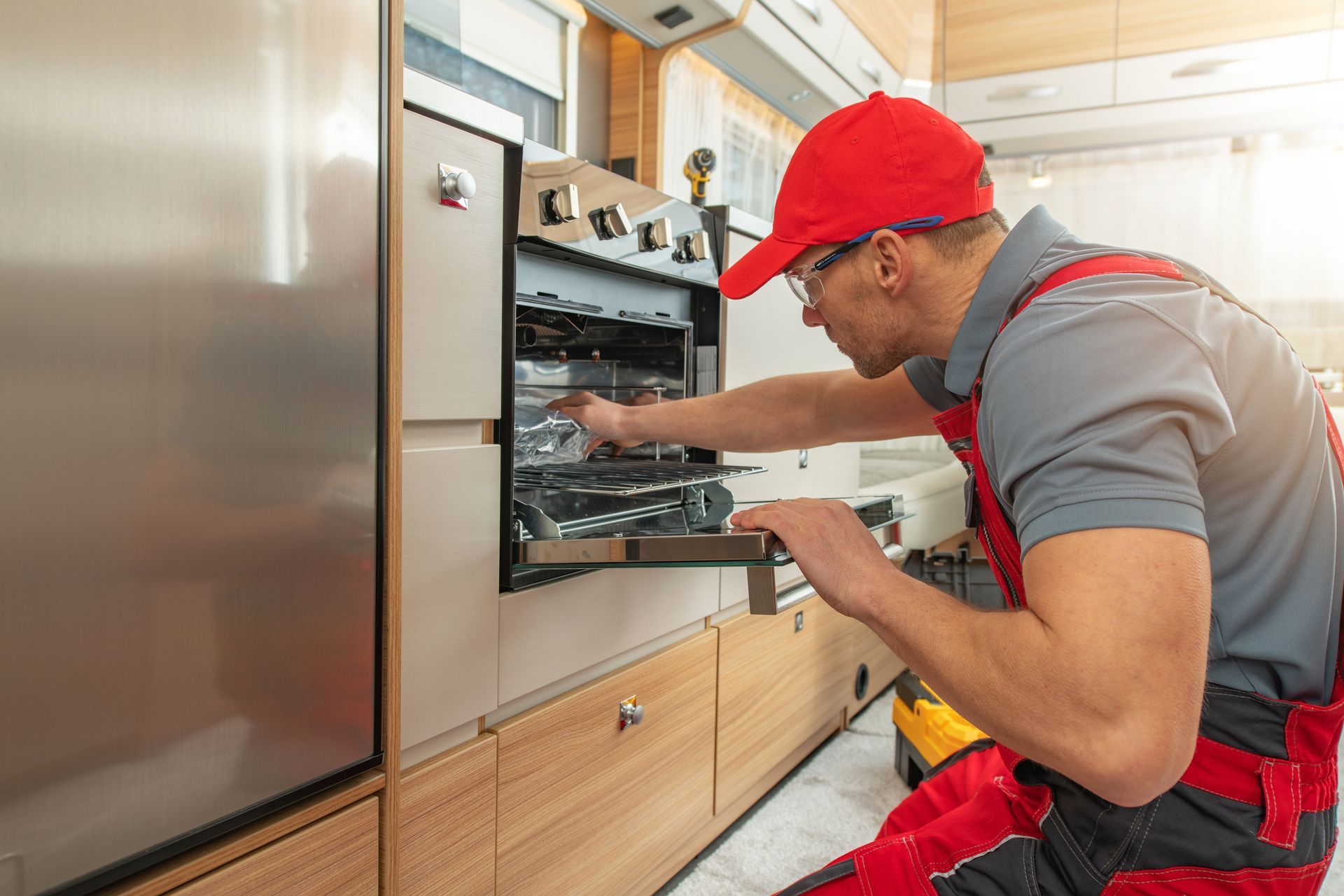 Technician in red cap inspecting an open built-in oven in a modern kitchen
